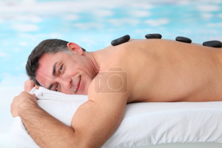 Man laying on massage bed with hot stones