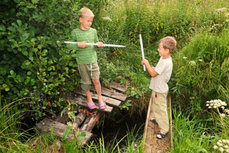 Two boys with sticks battling for fun on bridges over stream